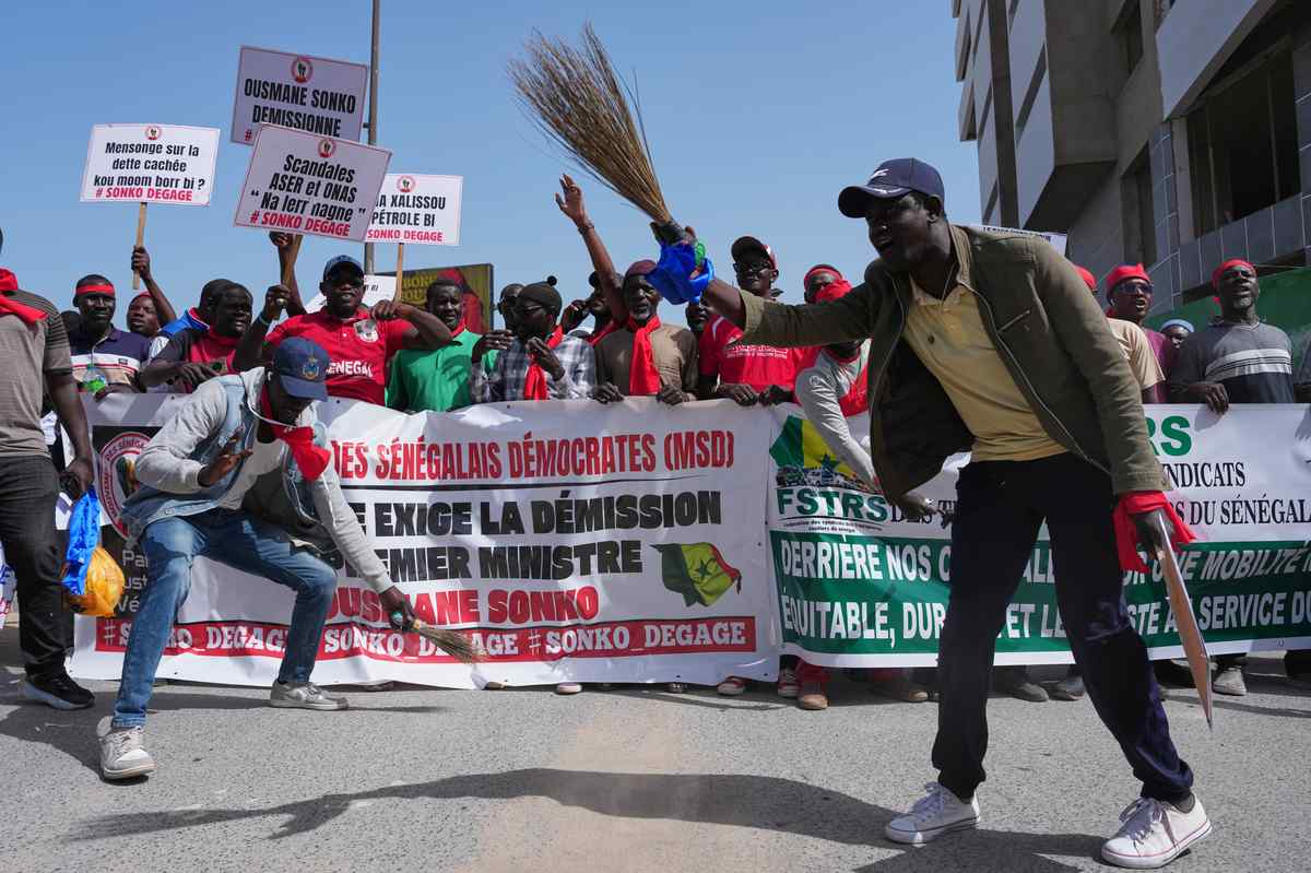 Hundreds of people marching in Dakar, Senegal, holding signs and wearing red scarves.