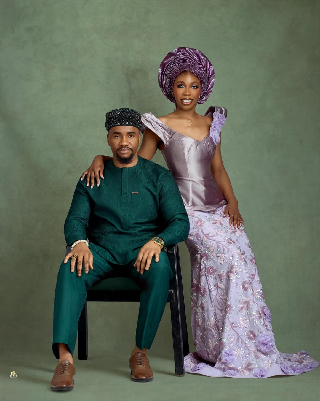 Nollywood actor Jide Kene Achufusi in a forest green Agbada and black beaded cap seated beside his bride, Ifeoma, who is wearing a lilac structured corset top and floral lace mermaid skirt for their pre-wedding photoshoot.