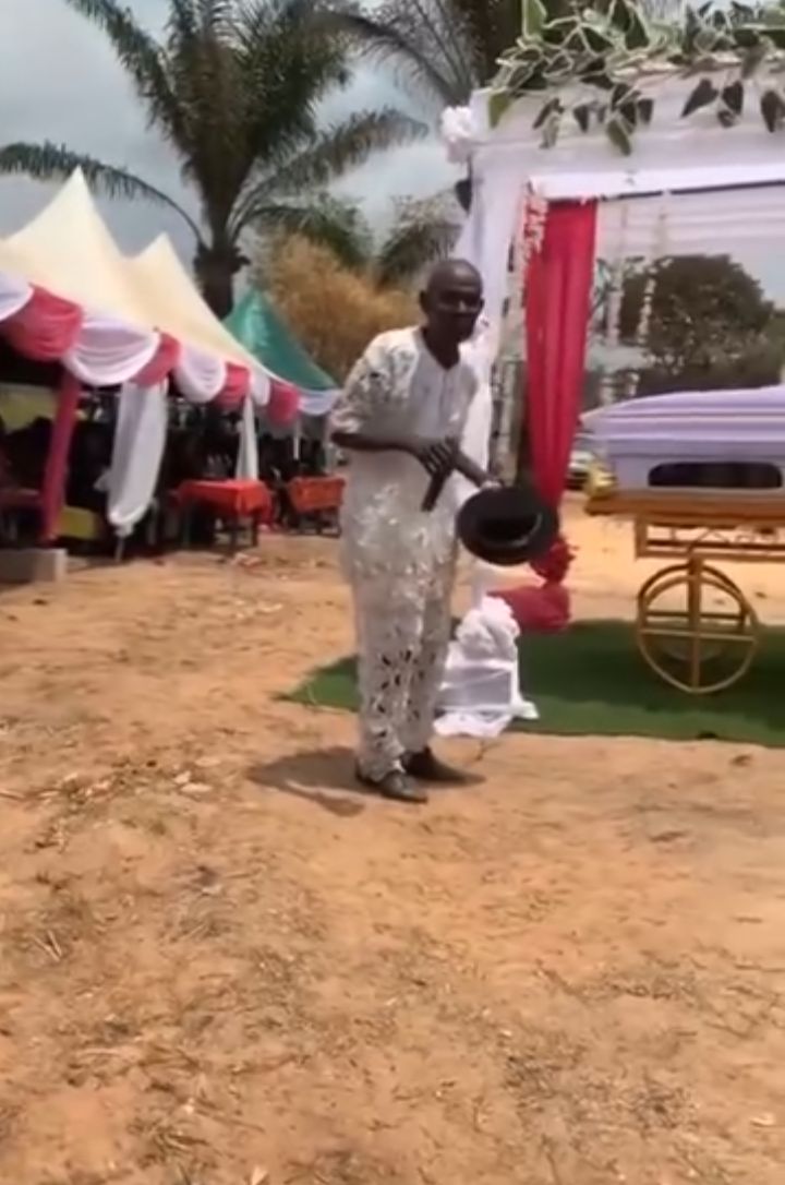 Elderly Nigerian man standing beside the coffin of his late daughter-in-law during her funeral.